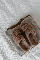 Cozy brown slippers on stack of warm wool pullovers and sweaters on white muslin cloth. Warm home wearing. Flat lay, top view