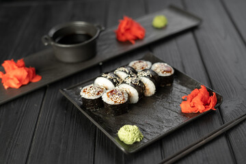 Japanese food concept. Maki sushi rolls with smoked eel, cucumber, sesame seeds, soy sauce, wasabi and ginger served on black background