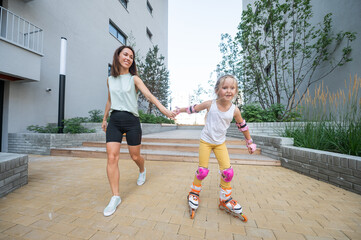 Mother helps daughter learn to roller skate. 