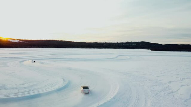 drone shot of two sports cars driving on a frozen lake during sunset in arctic circle