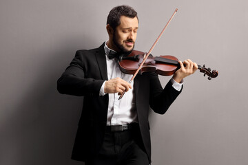 Man playing a violin and leaning on a gray wall