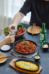 맛있게 만들어진 쭈꾸미 삼겹살이 차려진 한국의 식탁에서 술을 곁들이는 커플의 모습