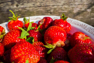 Close-up strawberry crop lying in a plate on rural wooden steps. The concept of healthy food, vitamins, agriculture, market, strawberry sale