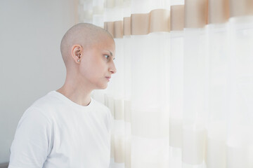 A young woman in her 30s with oncology who has lost her hair after chemotherapy stands by the...