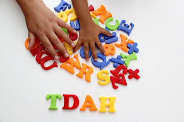 Hands of mom and daughter playing with colored letters that form ADHD Attention Deficit Hyperactivity Disorder in Spanish language - obrazy, fototapety, plakaty