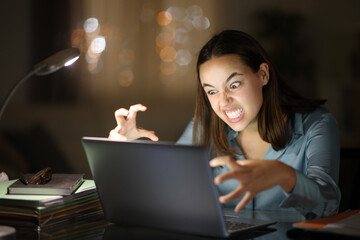 Angry teleworker using laptop in the night