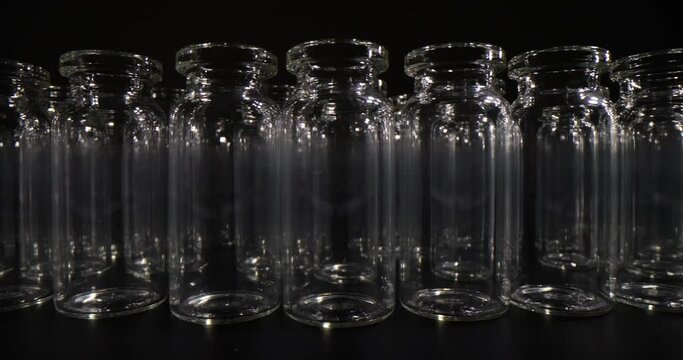Empty glass vials for vaccines stand in rows on table surface in dark studio. Professional glassware for medical purposes and laboratory investigations slow motion