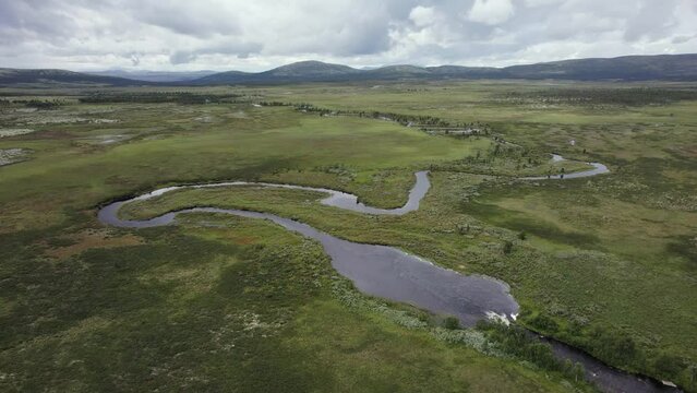 Small tundra river meanders through flat Norway landscape, aerial