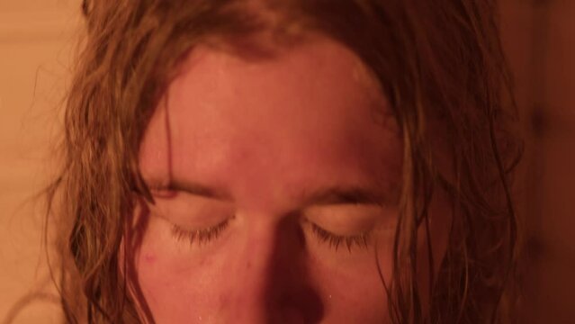 Close-up of a long-haired Finnish man's face in a wooden sauna. The man is sweating and enjoying the steam.