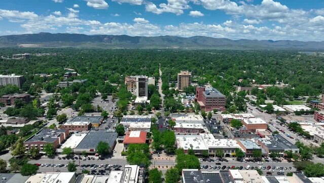 High descending shot of Fort Collins Colorado skyline. Beautiful summertime establishing shot. Green trees and mountain background on blue sky day.