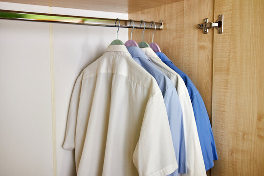 Plain men's shirts hang on a hanger in the closet.