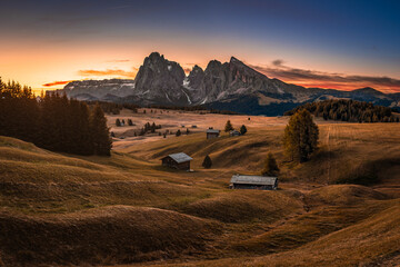 Alpe di Siusi, Italy - Seiser Alm, an alpine meadow on a warm autumn sunrise with Saslonch (Sassolungo or Langkofel) mountain of the Italian Dolomites and wooden cottages and colorful sky and clouds