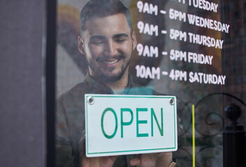 Shop, window and happy businessman open with sign for working time in retail, store or service in...