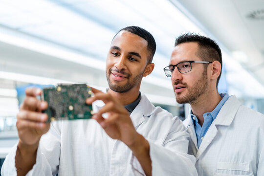 Two colleagues discussing over motherboard in electronics factory