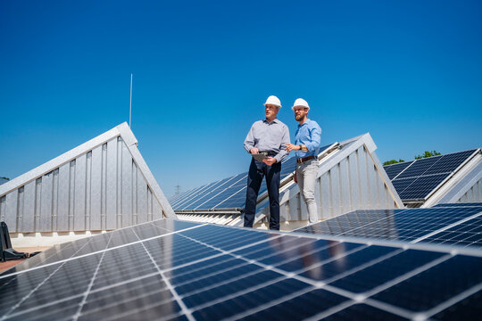 Two businessmen wearing hardhats having a meeting on the roof of a building with solar panels