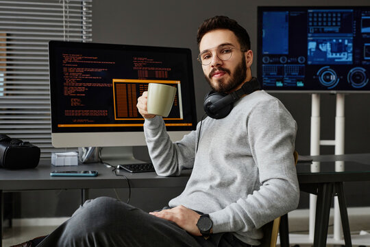 Computer programmer sitting with coffee cup in front of desktop PCs