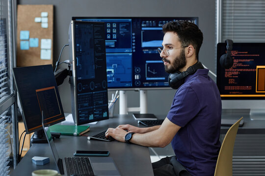 Young computer programmer with wireless headphones coding on desktop PC