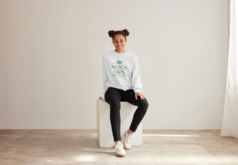 Mockup of woman wearing customizable color sweatshirt sitting on plinth, full length