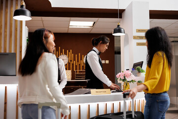 Cozy hotel reception with two female guests waiting for concierge to finalize booking procedure....