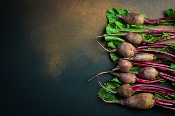 Raw organic beetroot and beetroot leaves, on a dark background, close-up, top view.
