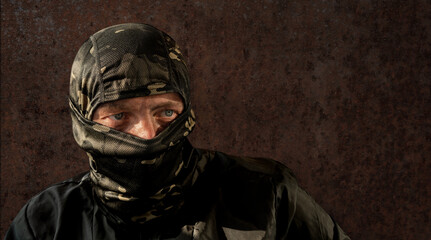 Military man with dirty face and camouflage mask. The concept of a person after military action or fraud, robbery. Close-up. A man on a dark background in a balaclava. Looking away.