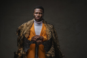 Portrait of a stylish dark-skinned man in a yellow jacket draped in a wild animal skin posing with...