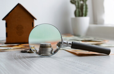 A magnifying glass, a toy house and banknotes lie on the table. Concept of money market, financial economy and real estate insurance.