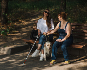 Blind caucasian woman sitting on bench with guide dog and pregnant friend. 