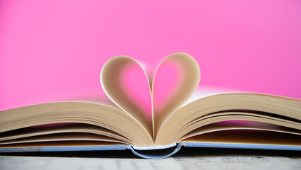 Heart from a book page on pink background, book of love