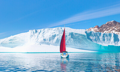 Giant iceberg near Kulusuk with lone yacht with red sails - Greenland, East Greenland