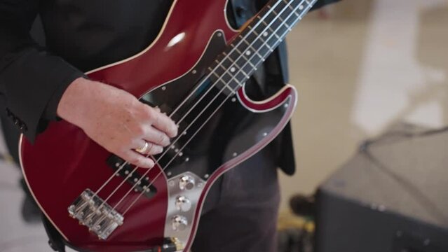 White Man's Hand Strumming Red Electric Bass Guitar Close Up