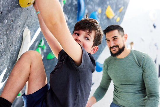 Boy climbing up a wall with his smiling dad