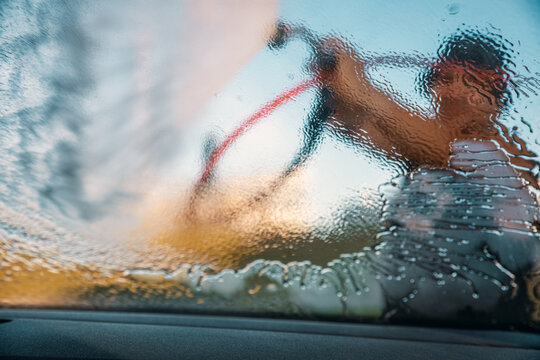 Man washing his car at an outdoor self-service  car wash station. View from inside of car