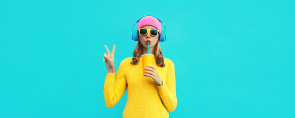Portrait of modern cool young woman listening to music in headphones and drinking fresh juice...