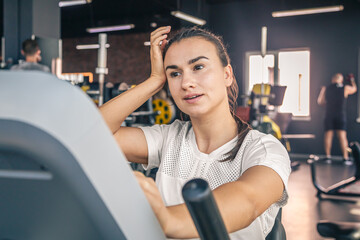 Fototapeta premium A tired young brunette woman in sportswear in the gym is engaged on a bike.