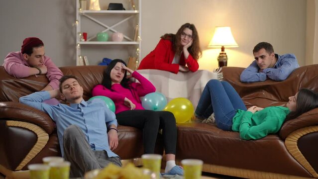 Wide shot group of bored young men and women in living room indoors. Careless Caucasian friends partying