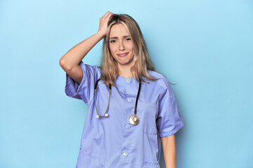Young caucasian nurse in blue studio being shocked, she has remembered important meeting.