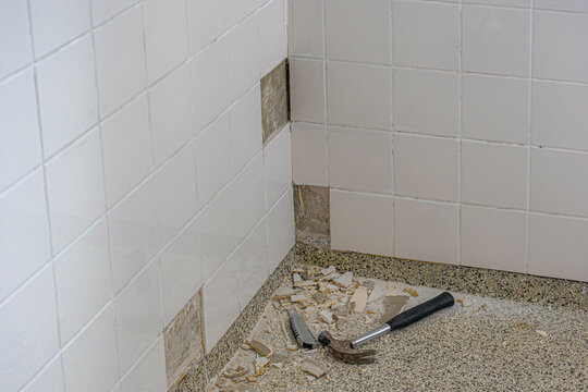 Renovation concept, Interior of old bathroom, Repair of broken white tiled on the wall in the shower room, Construction equipment with hammer and cutter on the granite floor.