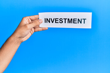 Hand of caucasian man holding paper with investment word over isolated blue background