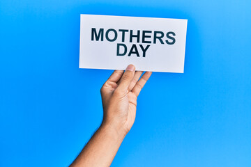 Hand of caucasian man holding paper with mothers day message over isolated blue background