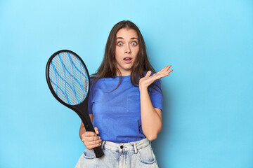 Woman with an electric bug zapper on a blue background surprised and shocked.