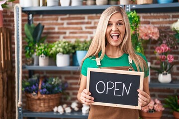 Young woman working at florist holding open sign smiling and laughing hard out loud because funny crazy joke.