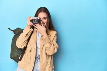 Traveling woman taking pictures with a vintage camera on blue.