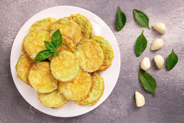 Baked zucchini with cheese, garlic and fresh herbs on a gray background.