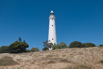 Beautiful old white lighthouse on Rottnest Island. Wadjemup Lighthouse at Rottnest Island, Western Australia. Tall white historic lighthouse on a hill in front of a perfect blue sky. 