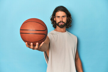 Long-haired, bearded man holding a basketball in a blue studio.