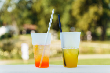 Two different summer cocktails in glasses with straws on a blurred green background
