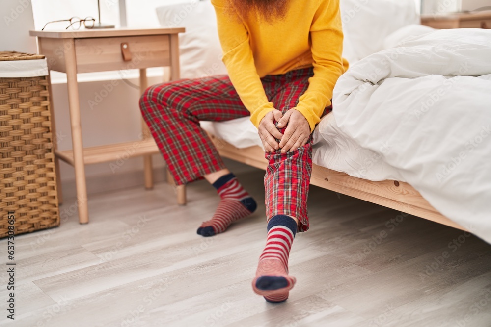 Sticker young redhead man suffering for knee injury sitting on bed at bedroom