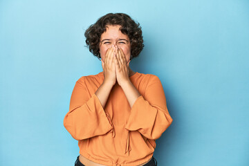 Young Caucasian woman with short hair laughing about something, covering mouth with hands.