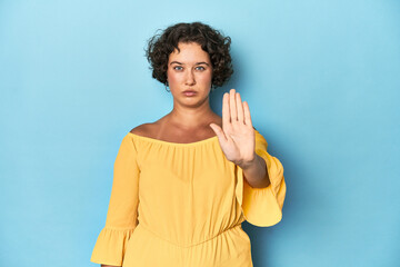 Young Caucasian woman with short hair standing with outstretched hand showing stop sign, preventing...